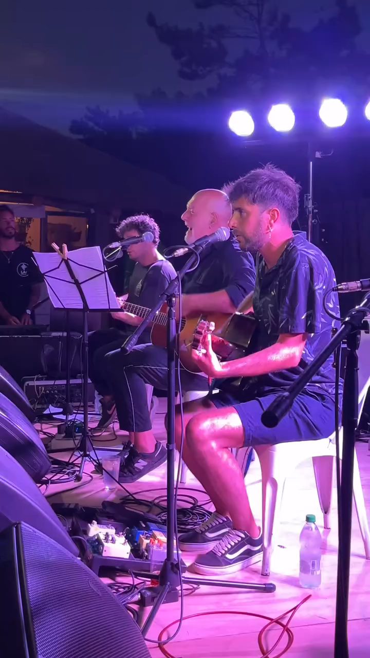 Banda completa tocando en el escenario con luces violetas